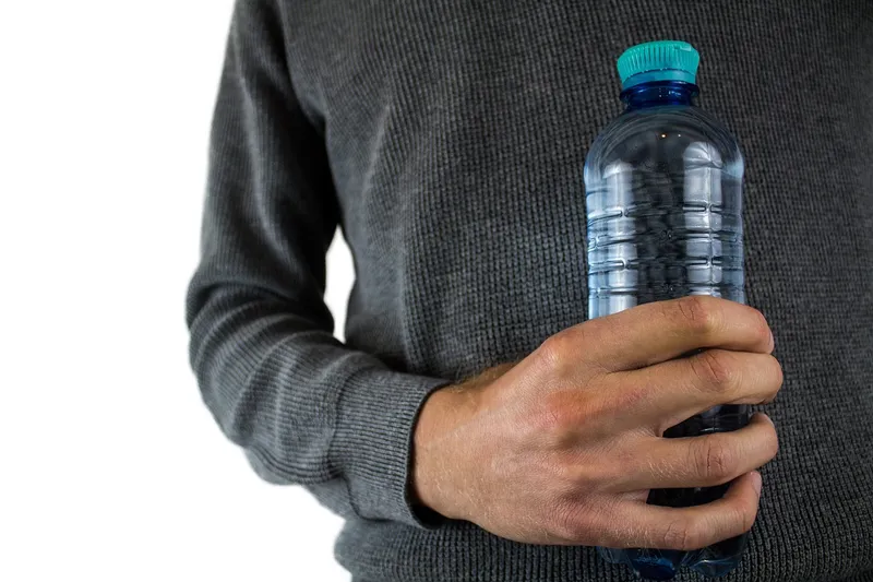 A clear plastic bottle with the bottom removed used as a mini greenhouse over a small plant.